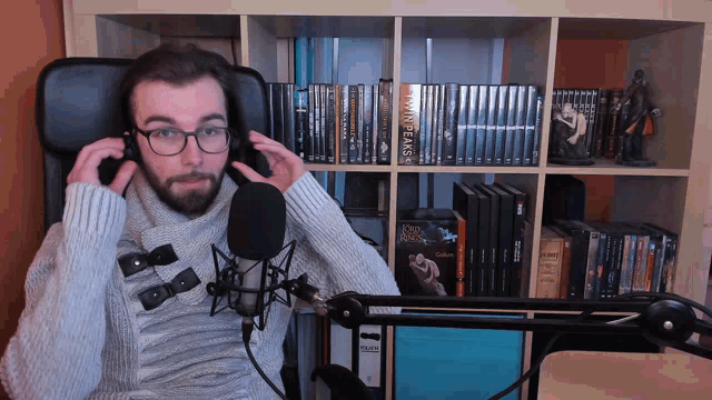 a man sitting in front of a microphone with a book called twin peaks on the shelf behind him