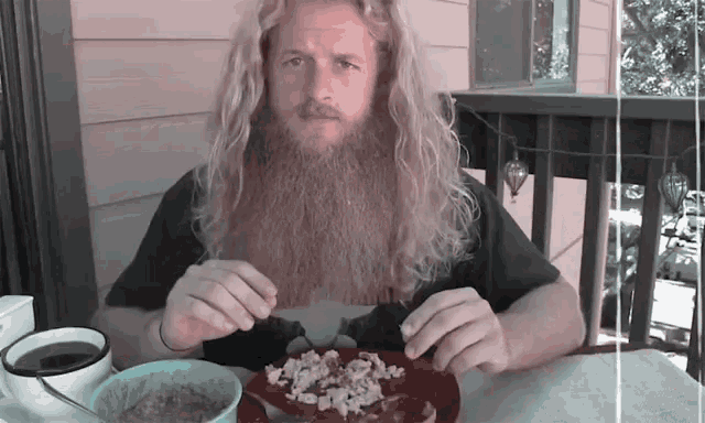 a man with a beard is sitting at a table with a plate of food