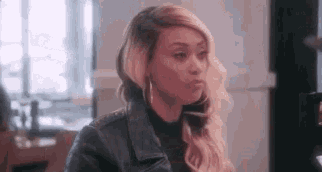 a woman wearing a leather jacket and earrings is sitting at a table in a room .