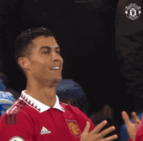 a soccer player wearing a red adidas jersey is smiling and clapping his hands .