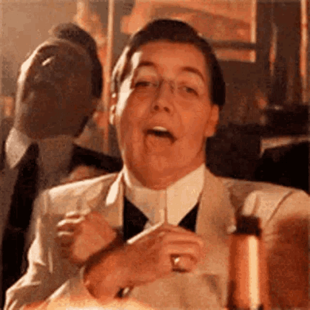 a man in a suit and tie is holding a glass of wine and smoking a cigarette .