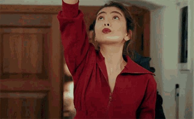 a woman in a red dress is standing in front of a door with her arm up .