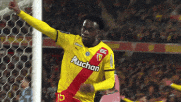 a soccer player wearing a yellow and red auchan jersey celebrates a goal