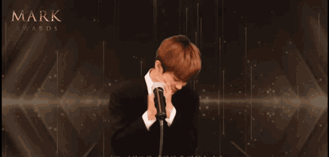 a man in a suit and tie stands in front of a microphone with the words mark awards on the bottom