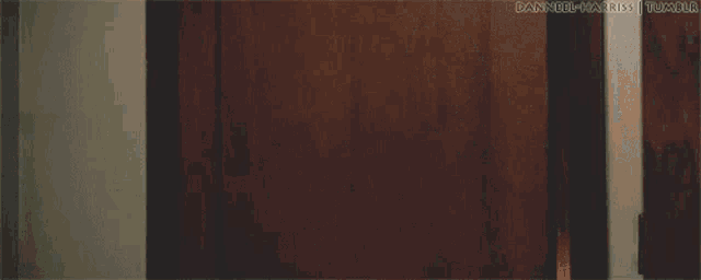 a woman in a grey shirt is standing in front of a door looking at the camera .