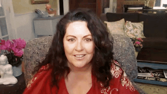 a woman in a red shirt is sitting in a chair smiling
