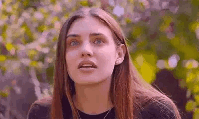 a close up of a woman 's face with a surprised look on her face in front of a tree .