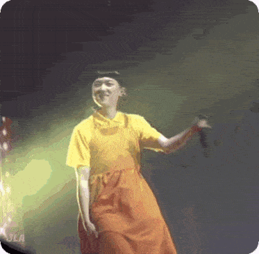 a man in a yellow shirt and orange dress is holding a microphone on a stage