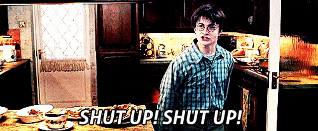 a man in a plaid shirt stands in a kitchen and says shut up shut up