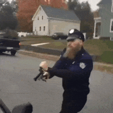 a police officer with a beard is holding a gun in his hand while walking down the street .