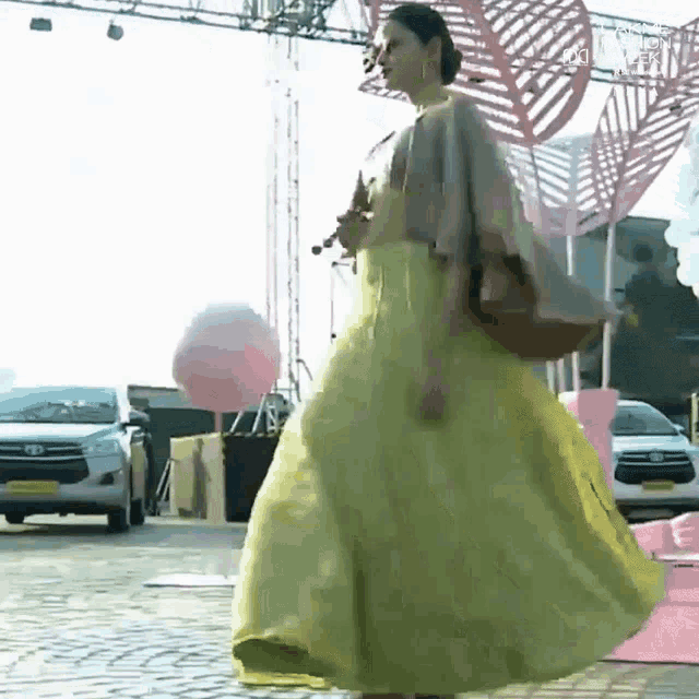a woman in a long yellow dress is walking down a street .