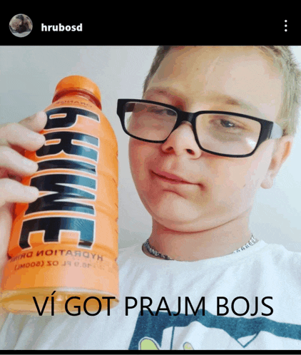 a boy wearing glasses is holding a bottle of orange drink that says " prime "