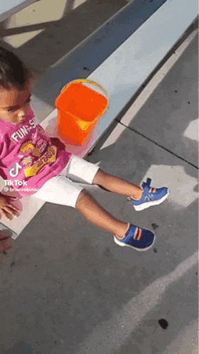 a little girl is sitting on a bench with her legs crossed and a toy bucket in the background .