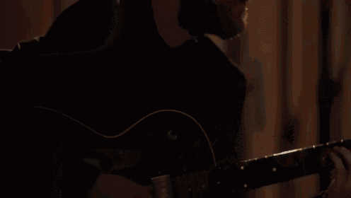 a man in a black coat is singing into a microphone in a recording studio .