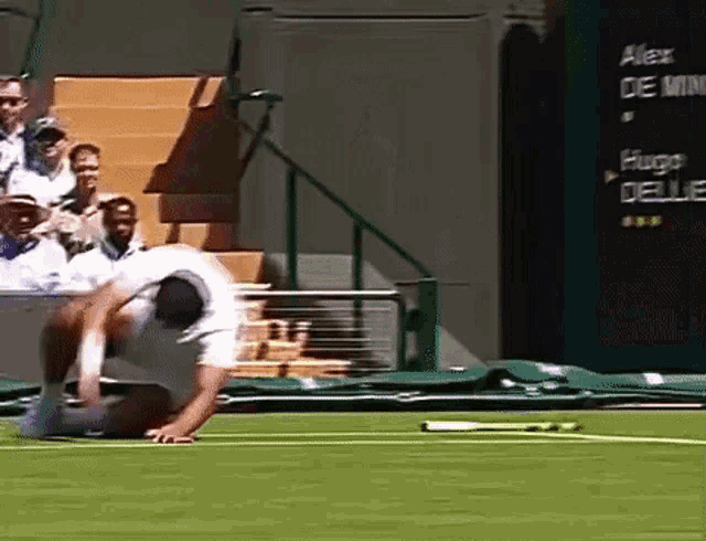 a man is kneeling down on a tennis court with a scoreboard behind him that says alex de uce