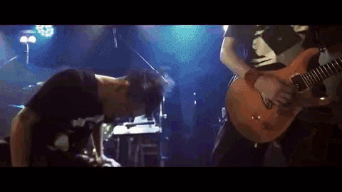 a man playing a guitar and another man playing drums on a stage