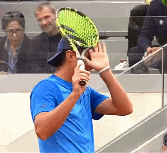 a man in a blue shirt is holding a tennis racket
