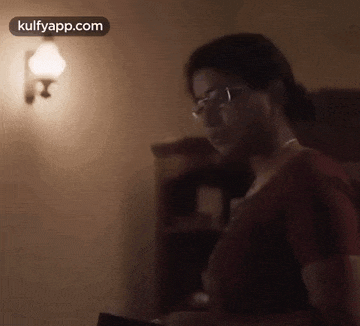 a woman wearing glasses is standing in a dark room looking at something .