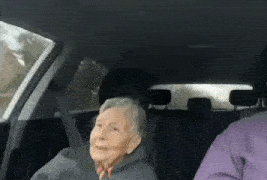 an elderly woman is sitting in the back seat of a car and smiling .