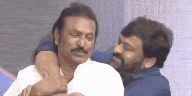 two men are hugging each other and laughing while sitting next to each other on a couch .