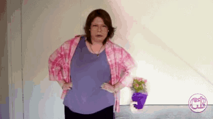 a woman is standing in front of a wall with her hands on her hips and a potted plant in the background .