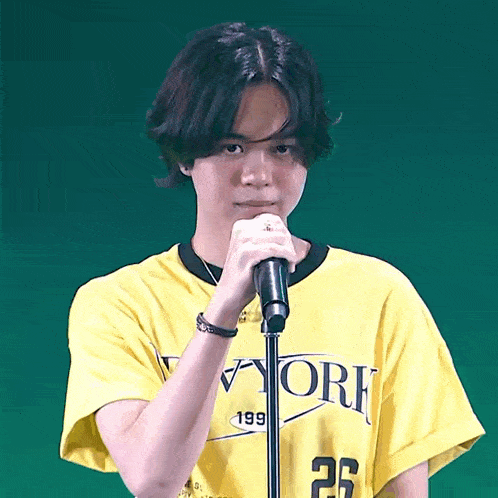 a young man wearing a yellow new york t-shirt holds a microphone