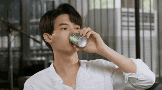 a man in a white shirt is drinking a can of soda