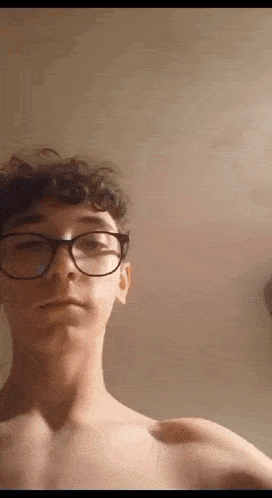 a young man without a shirt is wearing glasses and taking a picture of himself .
