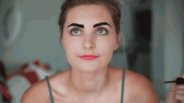 a woman is applying makeup to her eyebrows and looking at the camera .