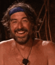a shirtless man with a beard is smiling and wearing a blue headband .