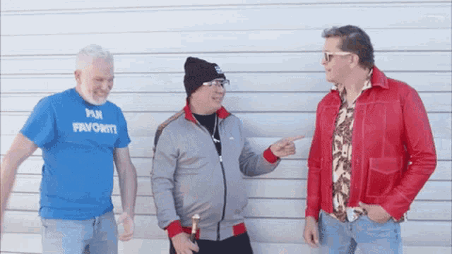 a man wearing a blue shirt that says fun favorite points to another man in a red jacket