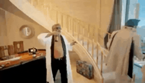 a man in a lab coat is standing next to a staircase in a room .