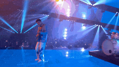 a man is playing a guitar on a stage with a drum set in the background