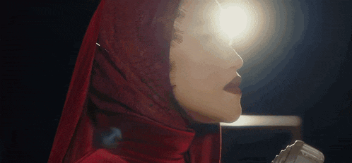 a woman wearing a red veil is singing into a microphone .