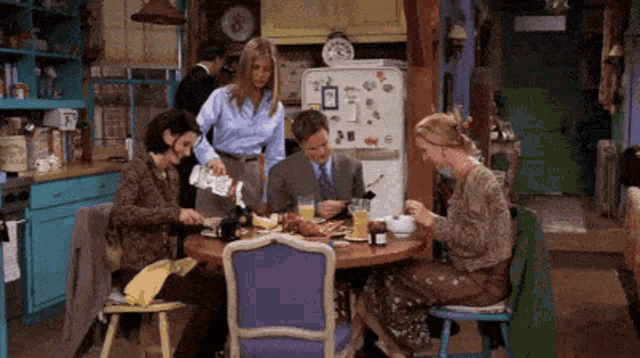 a group of people are sitting around a table with a refrigerator that has a magnet on it