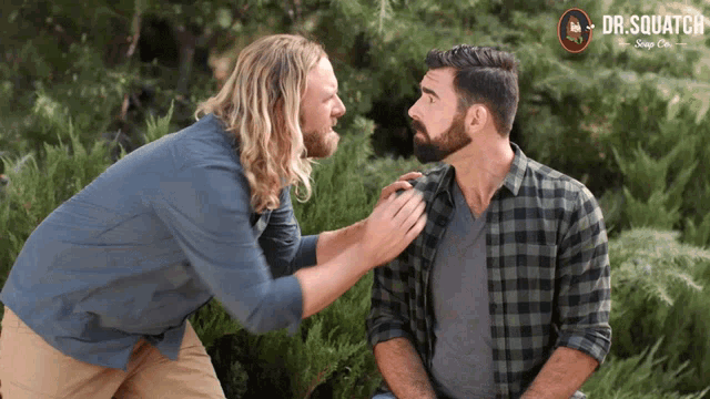 a man with a beard talks to another man with a dr.squatch logo in the background