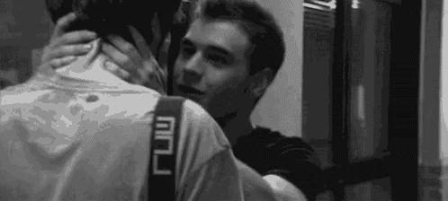 a black and white photo of two men hugging each other in a room .