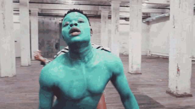 a man with green paint on his face is standing in a warehouse