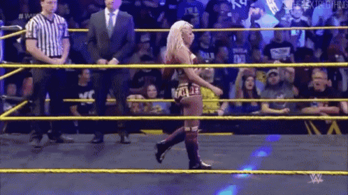 a woman is walking out of a wrestling ring while a referee looks on .