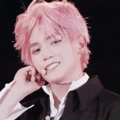 a young man with pink hair is smiling and holding his hand to his face