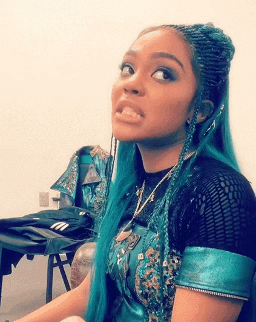 a woman with blue hair and braids is making a silly face