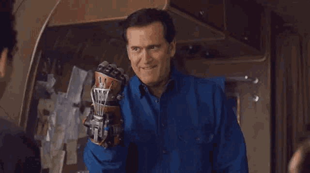 a man in a blue shirt is holding a robotic glove in his hand .