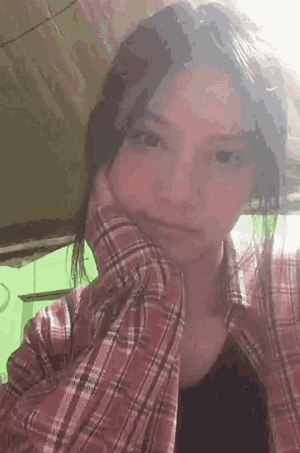 the girl is wearing a plaid shirt and a black tank top and is looking at the camera .