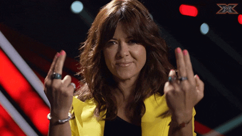 a woman in a yellow jacket giving the middle finger in front of an x factor logo