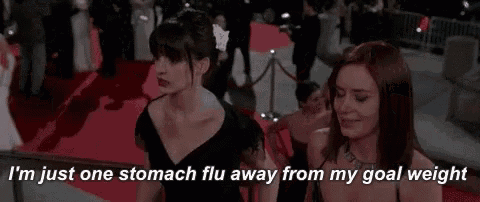 two women are standing next to each other on a red carpet . one of the women is talking about her stomach flu .