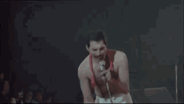 a shirtless man is singing into a microphone on a stage while holding a hula hoop .