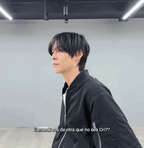 a man in a black jacket is standing in a room and talking to someone in spanish .