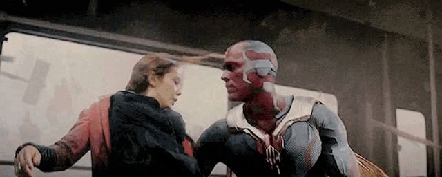 a man in a superhero costume is standing next to a woman in a red jacket .