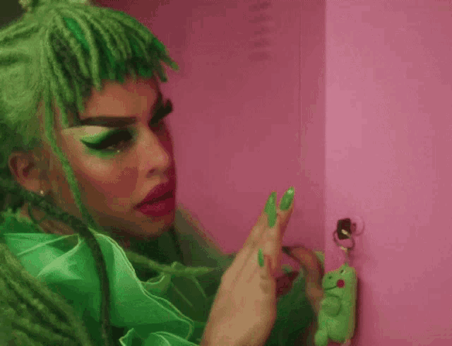 a woman with green hair is standing next to a pink wall with a frog keychain