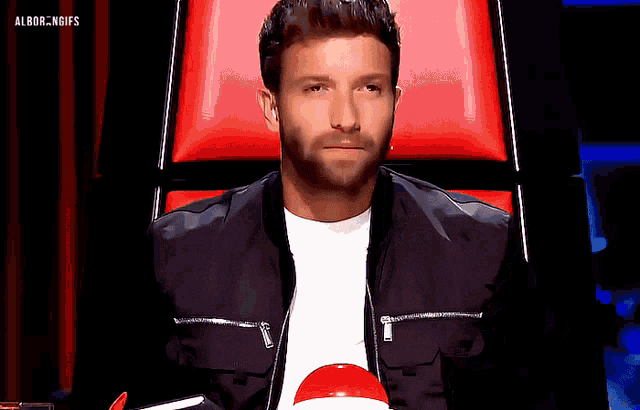 a man in a black jacket sits in a red chair with the words albor.ngifs on the bottom